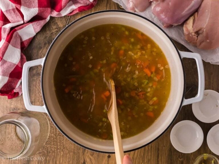 Using a wooden spoon to stir the broth and vegetables in a pot.