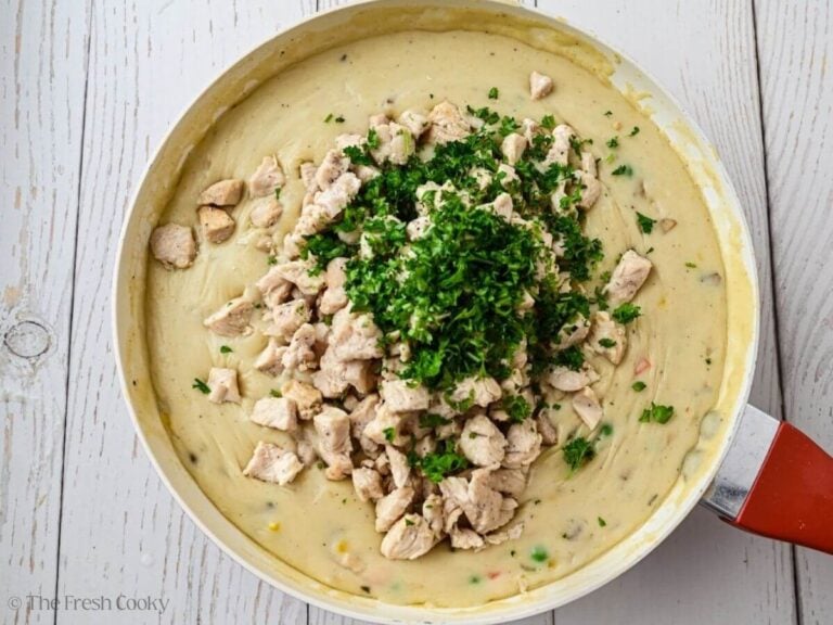 Chopped chicken and parsley added to the chicken pot pie filling in a skillet.