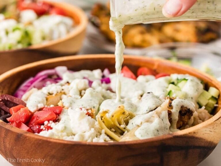 Tzatziki sauce being poured over the top of a Greek chicken bowl.