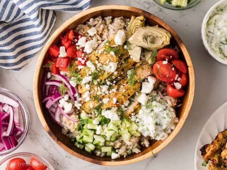 A greek chicken bowl, with all of the fixings including tzatziki sauce, cucumbers, artichoke hearts, tomatoes, red onions.