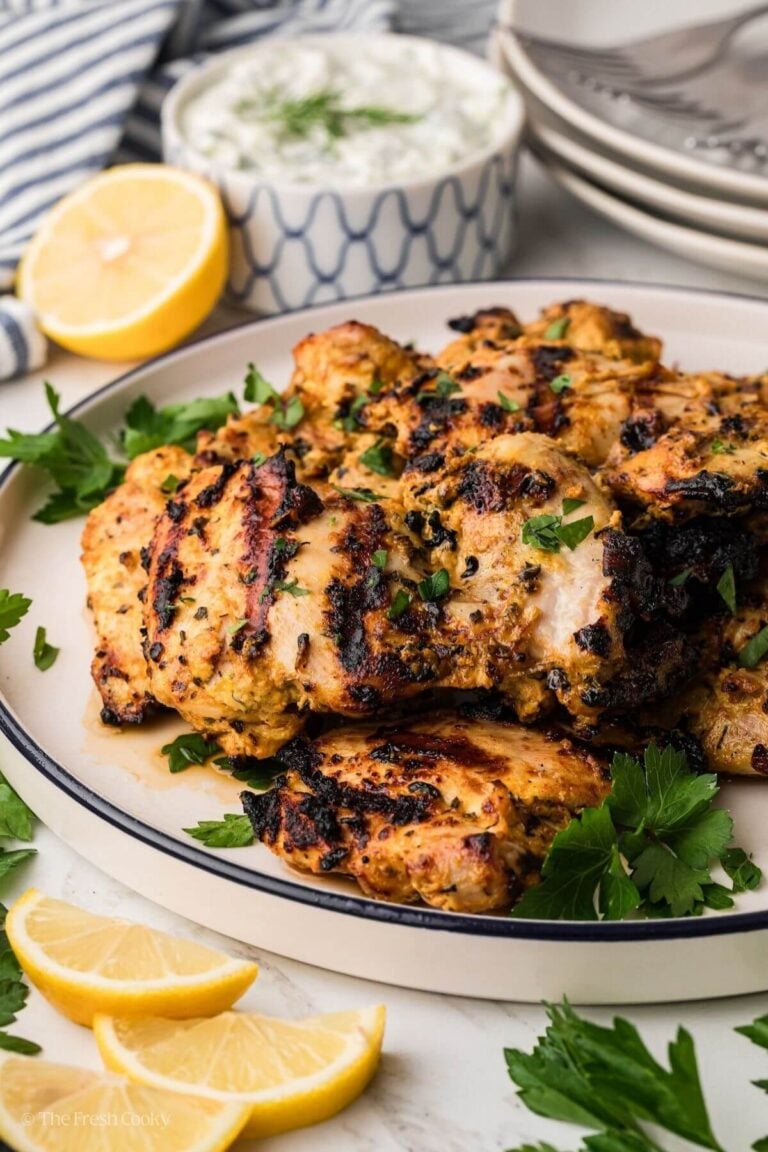 Marinated and grilled Greek Yogurt Chicken Thighs on a plate with lemons behind.