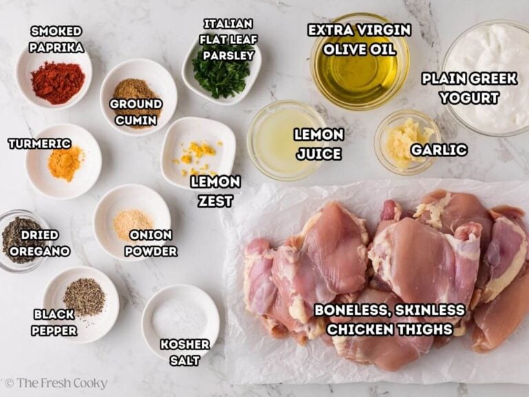 Greek yogurt chicken marinade ingredients, labeled L-R smoked paprika, cumin, parsley, olive oil, Greek yogurt, garlic, boneless, skinless chicken thighs, kosher salt, black pepper, turmeric, onion powder, lemon zest and lemon juice.