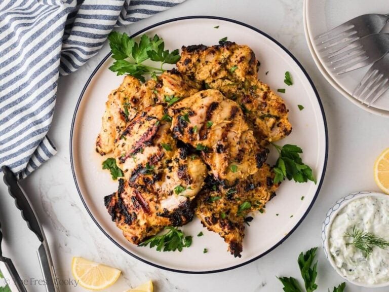 A white and blue plate with grilled chicken piled high and topped with fresh parsley.