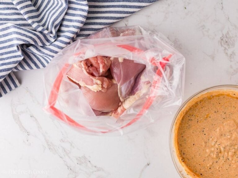 Boneless skinless chicken thighs in a plastic baggie with marinade in bowl.
