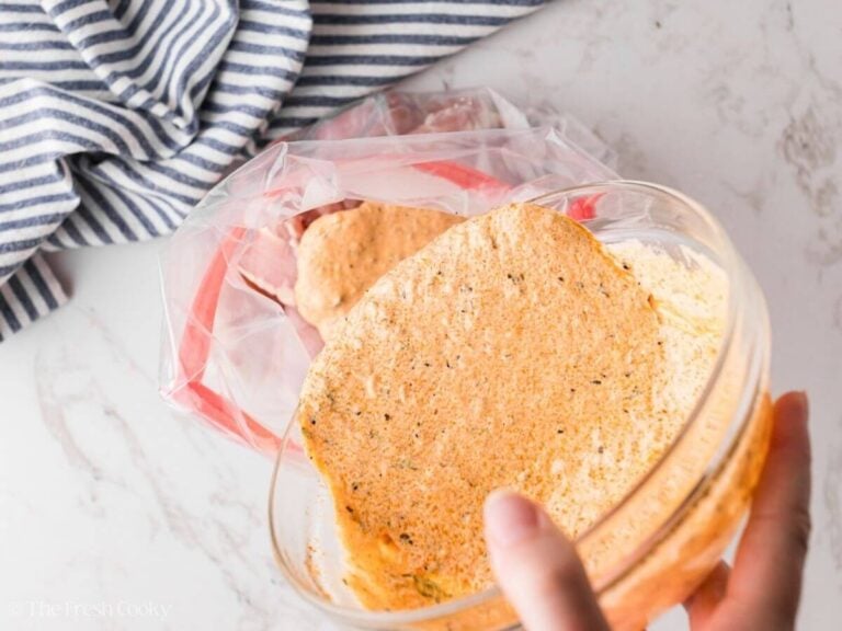 Hand pouring marinade into baggie over chicken.