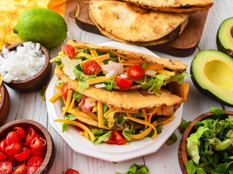 Two ground beef tacos served on a plate with lettuce, tomatoes and cheese on top.