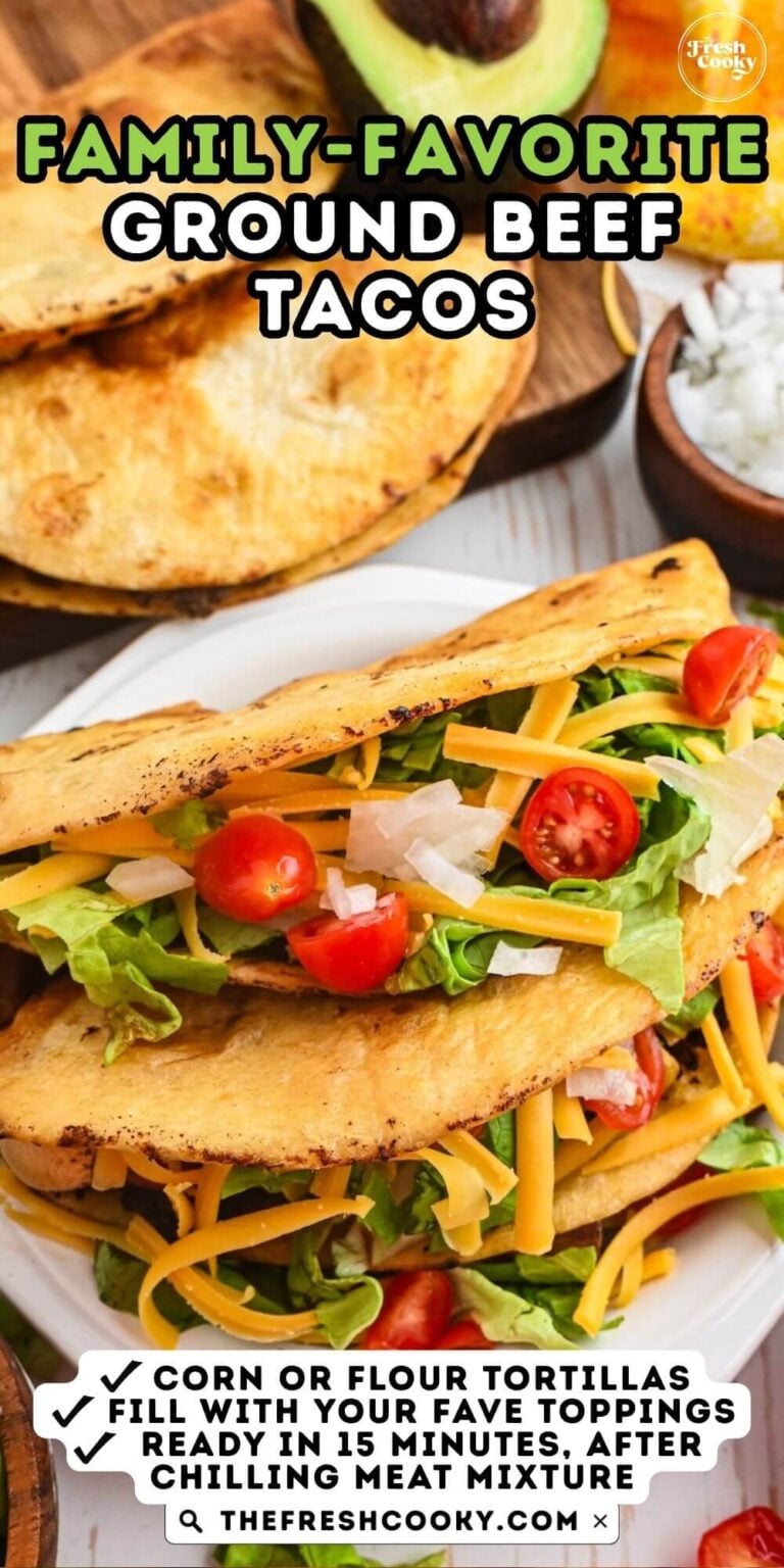 Two Mexican tacos filled with shredded lettuce, tomatoes, cheese and onions, on a plate, to serve. For pinterest.