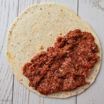 Taco seasoned ground beef pressed on top of half of a tortilla.