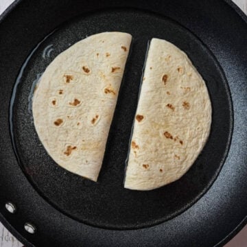 Two ground beef tacos in oil in a skillet.