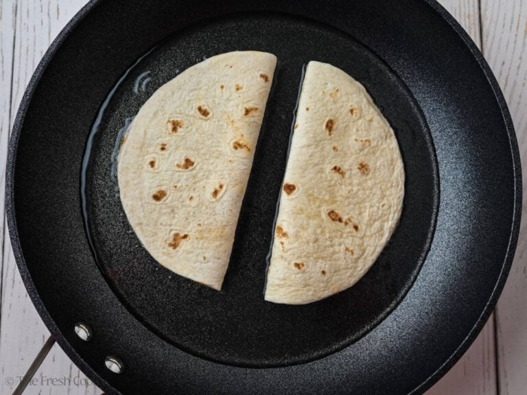 Two ground beef tacos in oil in a skillet.
