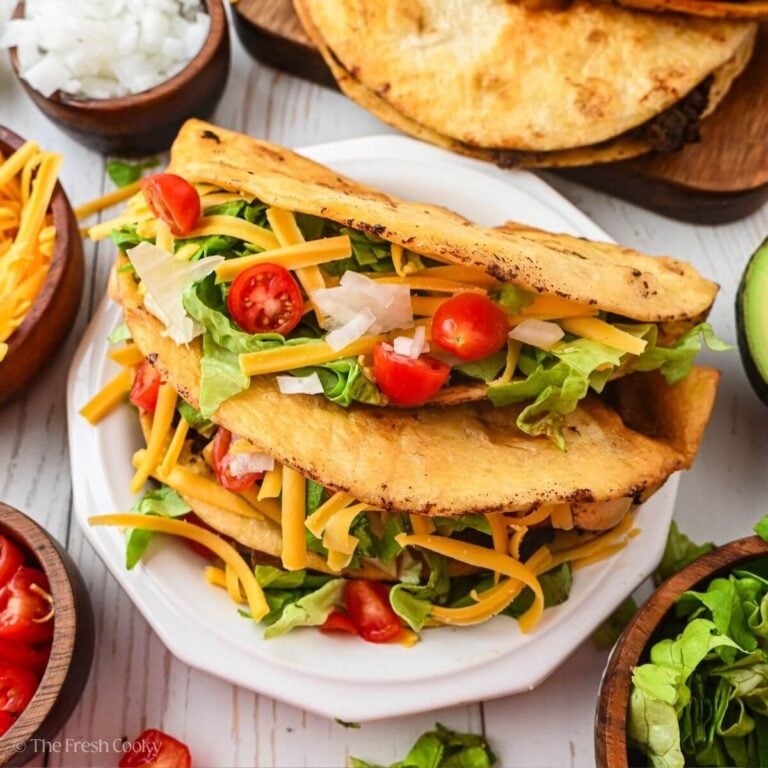 Two ground beef tacos on a plate with toppings.