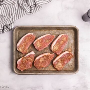 Pork chops on a sheet pan with spices sprinkled on top.