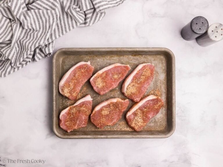 Pork chops on a sheet pan with spices sprinkled on top.