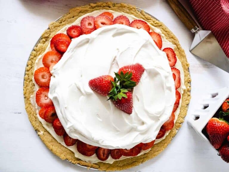 Fresh strawberries sliced on top of a cream topping on a sugar cookie crust, topped with fresh whipped cream and more strawberries, for this strawberry pizza recipe.