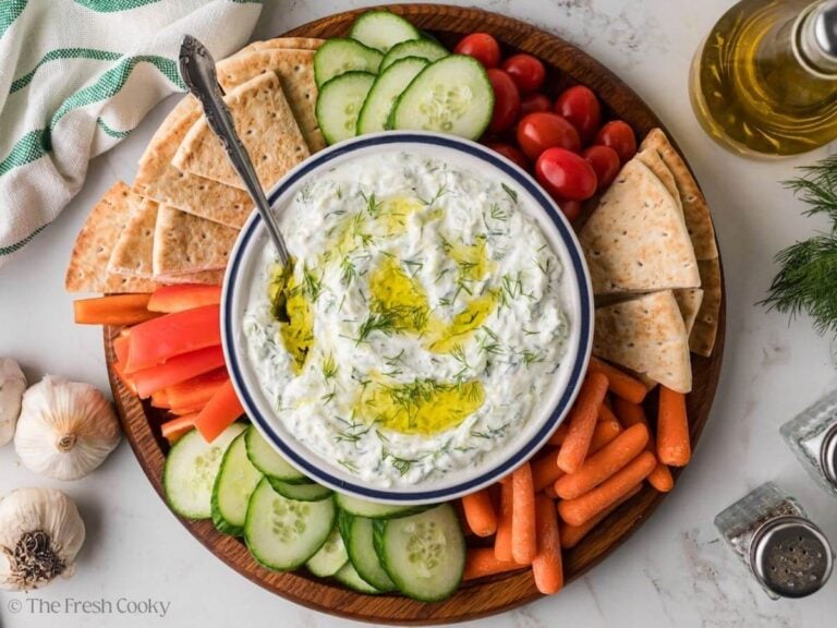 Overhead shot of tzatziki sauce in a bowl served on a platter with fresh vegetables and pita wedges.