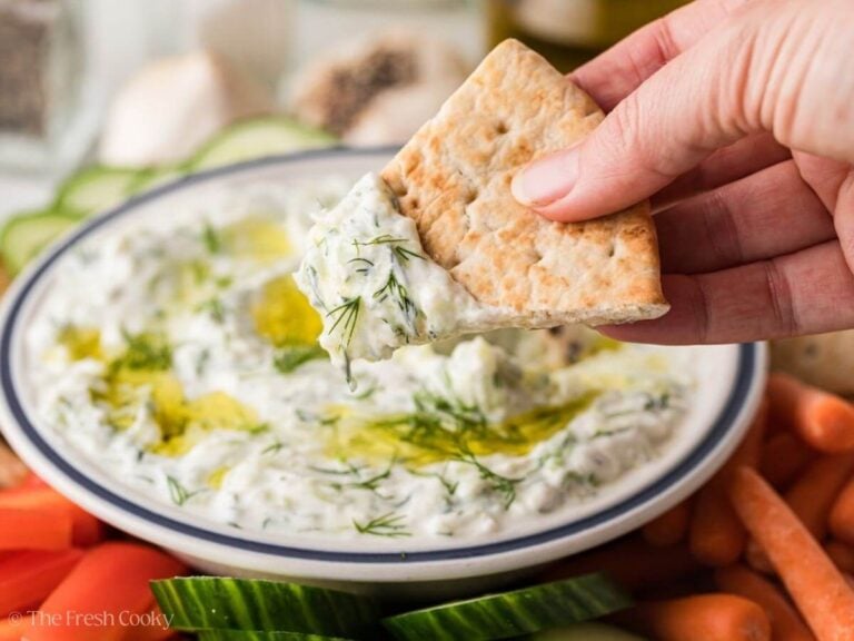 Hand holding a pita wedge with tzatziki sauce on it.