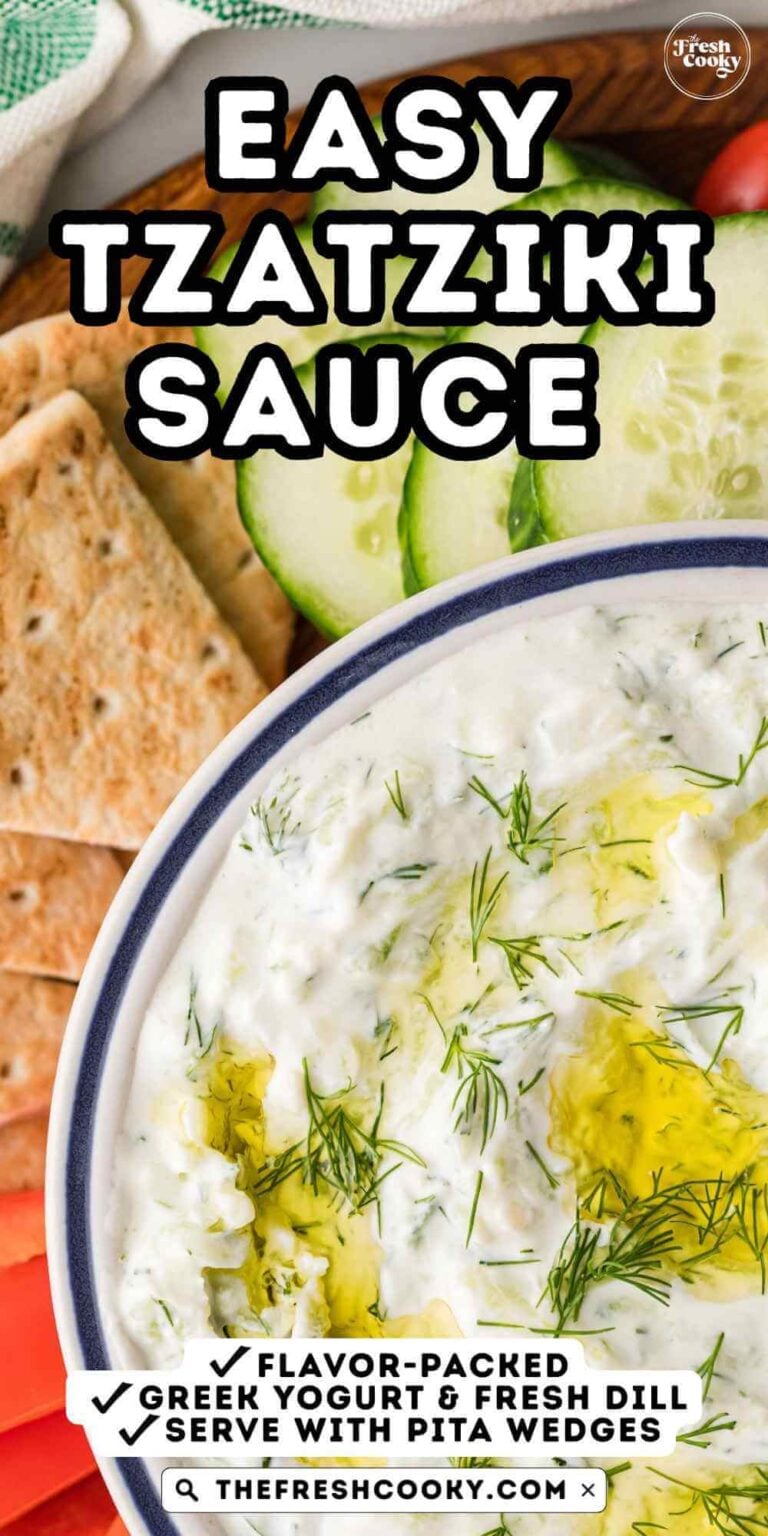 A close-up of a bowl of creamy tzatziki sauce surrounded by pita wedges and fresh vegetables. For pinning.