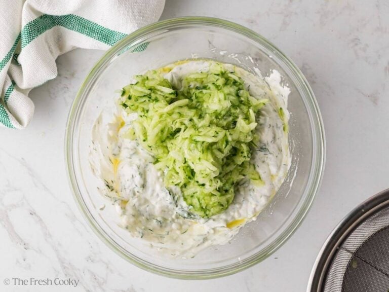 Grated cucumber added to the Greek yogurt mixture in a bowl.
