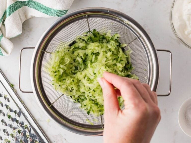 Salting the grated cucumber sitting in a fine mesh sieve.