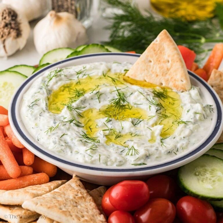 Side view of a bowl of tzatziki on a platter of vegetables and pita wedges.