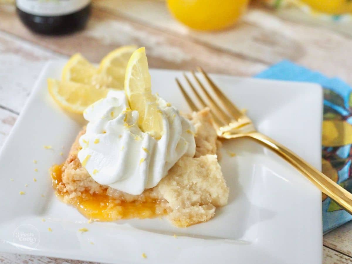 Lemon Dump Cake served on a plate with a swirl of whipped cream, and a gold fork.