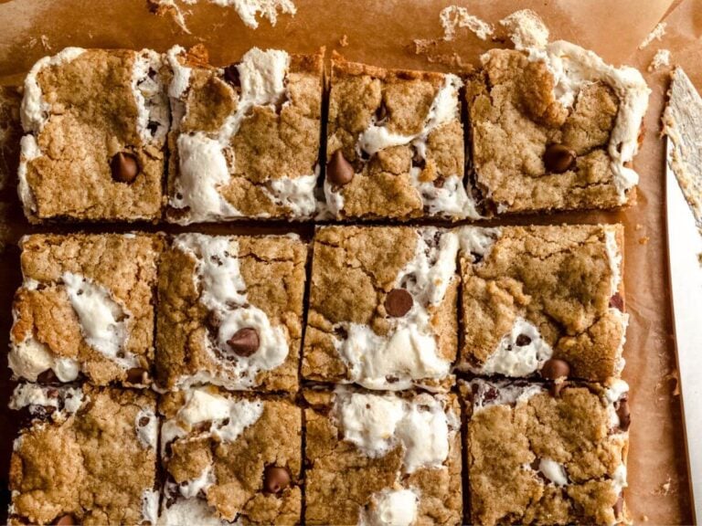 S'mores cookie bars sliced on a cutting board, with a gooey knife nearby.