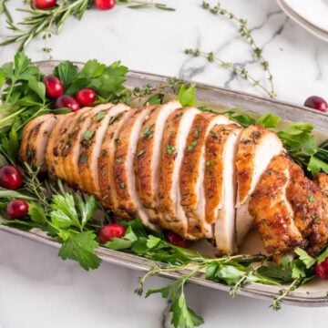 Sliced turkey breast on a serving platter with herbs and cranberries.