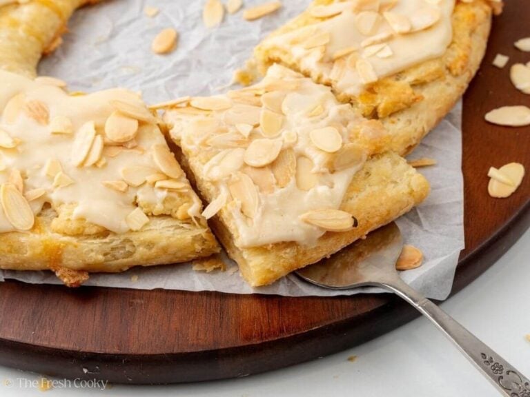 Metal spatula picking up a slice of almond kringle from a wooden board.