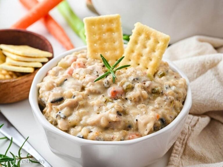 Bowl of chicken and wild rice soup with two crackers sticking out of it.
