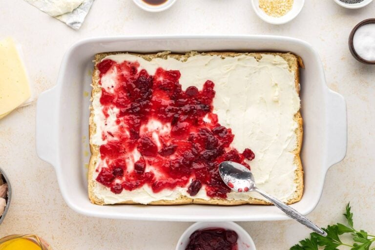 Whole cranberry sauce being spread onto cream cheese for easy baked turkey sliders.