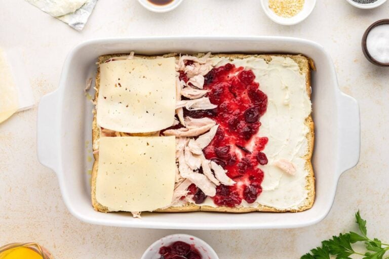 Easy baked turkey sliders with cream cheese, cranberry sauce, turkey and cheese layers shown.