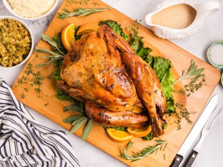 Overhead shot of an herb butter turkey placed on a bed of herbs on a wooden board.