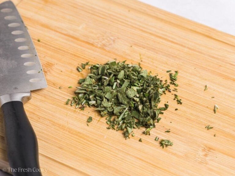 Diced fresh herbs on a cutting board next to a knife.