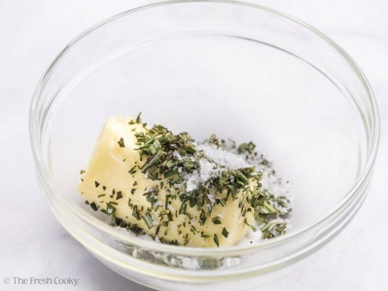 Salt and chopped herbs added to butter in a bowl.