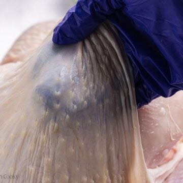 Using a hand to lift the skin from the turkey breast on a whole turkey.