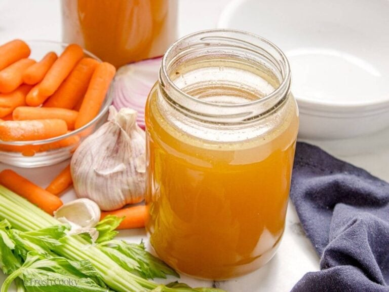 Jar of homemade chicken stock next to fresh vegetables.