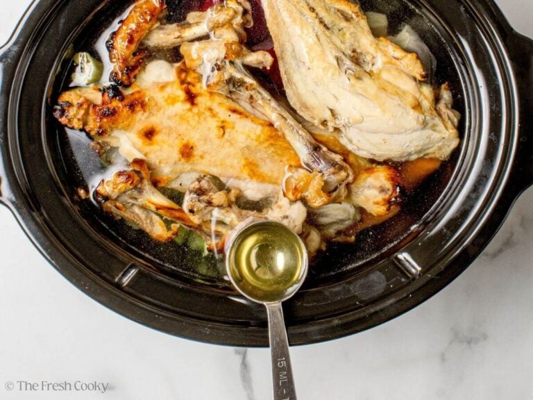 Apple cider vinegar being added to the broth ingredients in a slow cooker.