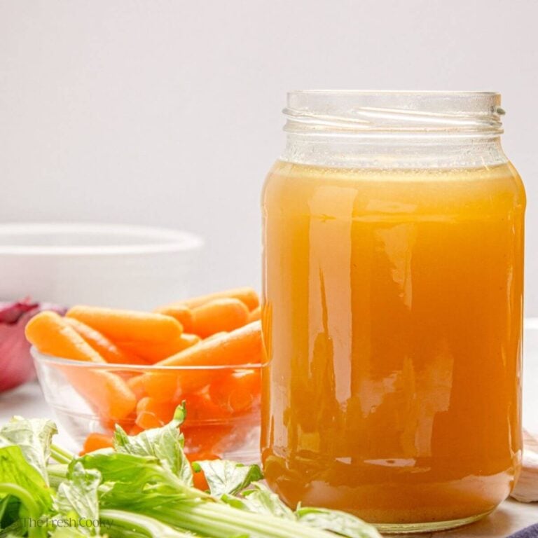 Side view of a jar of slow cooker chicken broth next to vegetables.