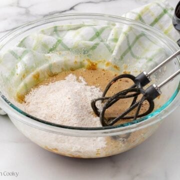 Dry ingredients being added to the wet ingredients in increments in a bowl.