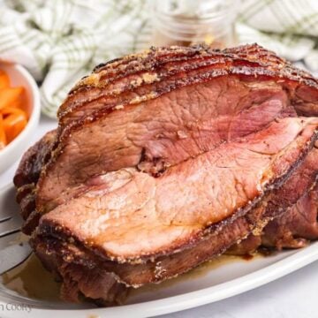 Spiral honey glazed ham, on a platter, with slices of ham separating, showing a sugary crust.