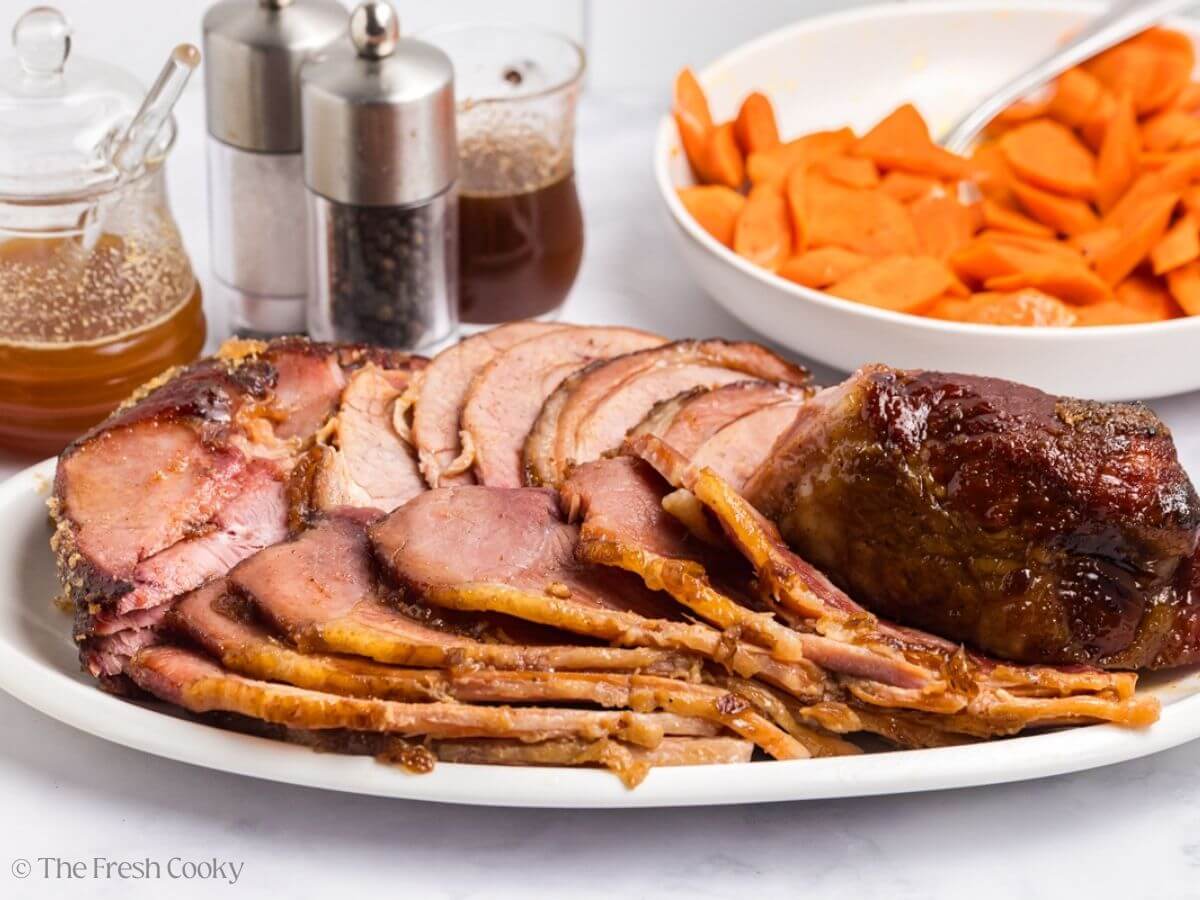 Platter with sliced spiral ham with veggies behind and some salt and pepper shakers.