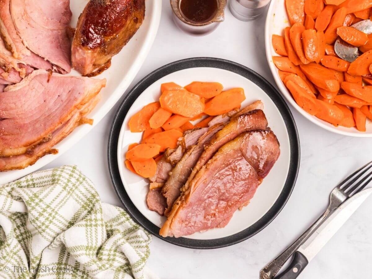 A plate with a serving with several slices of spiral ham on a plate with sliced carrots.