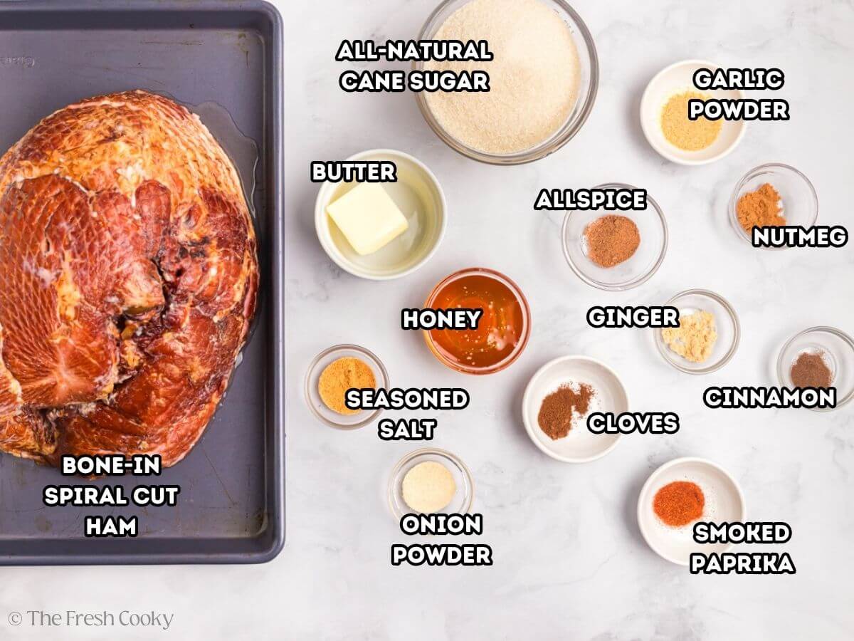 Labeled ingredients for how to cook a spiral ham, L-R spiral sliced ham, all-natural cane sugar, garlic powder, nutmeg, cinnamon, smoked paprika, onion powder, seasoning salt, butter, allspice, ginger, cloves and honey.