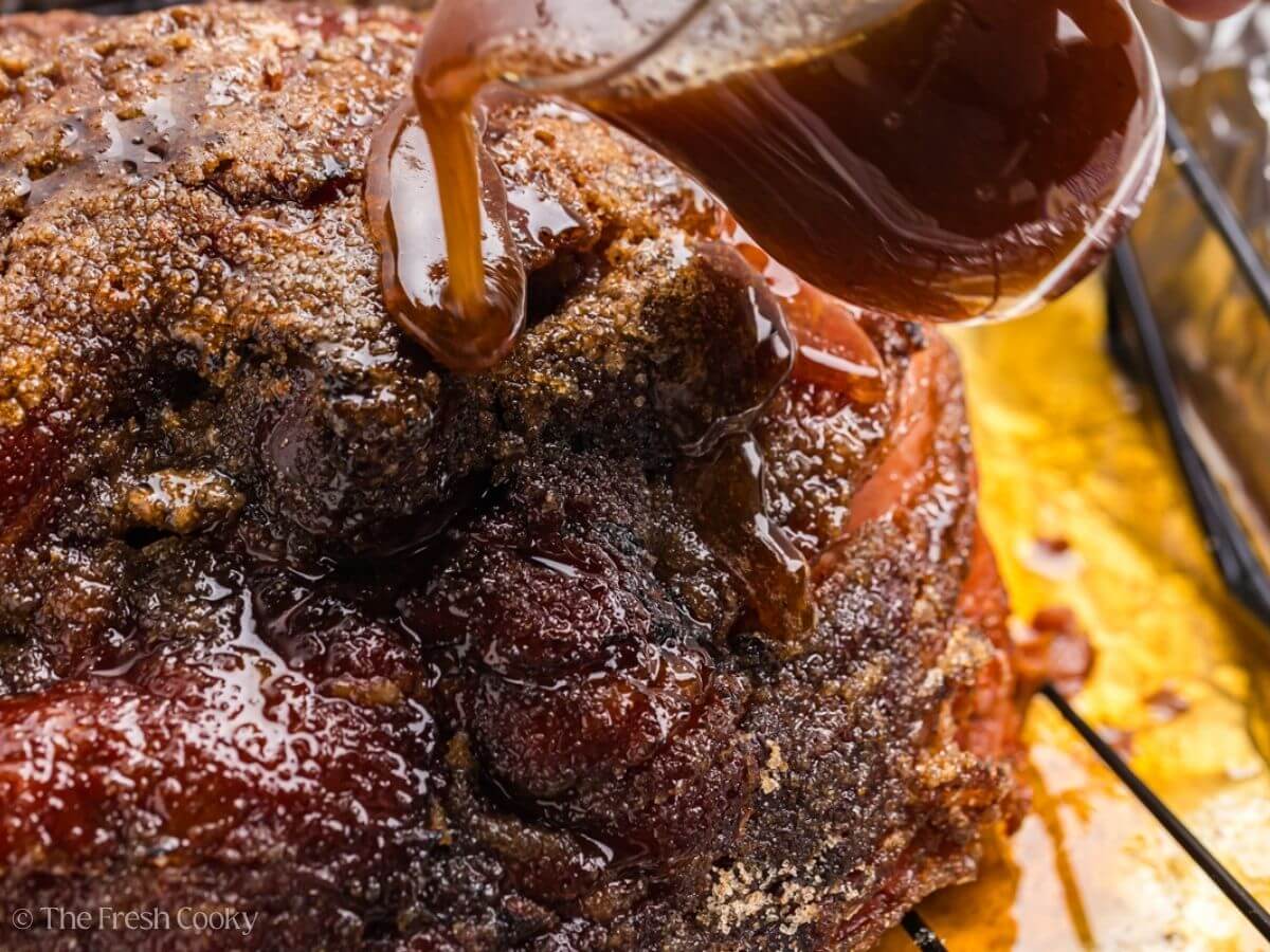 Pouring glaze on top of spiral sliced ham in a roaster.