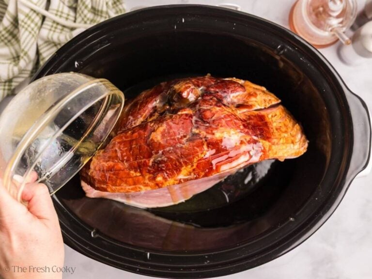 Spiral sliced ham in slow cooker, pouring honey butter mixture over the top and between slices.