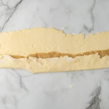 Almond paste being wrapped in the almond kringle pastry dough, one half first.