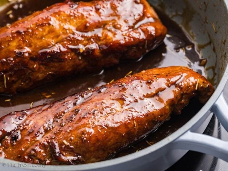 Two maple dijon pork tenderloins in a skillet coated in sauce.