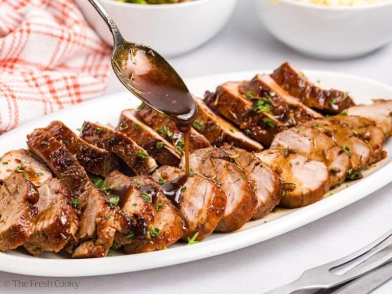 Spooning a maple glaze onto the sliced pork tenderloin on a serving dish.