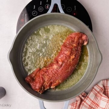 Pork tenderloin added to a skillet with butter in it.