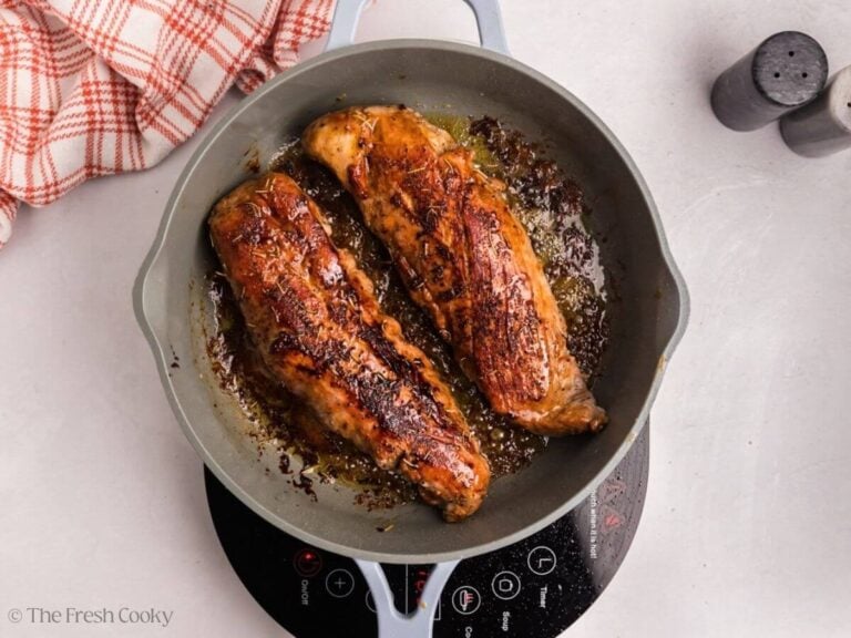 Two pork tenderloins searing in a skillet.